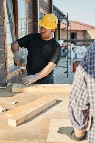 Man in Black Crew Neck T-shirt and Yellow Hard Hat Holding Gray Metal Hand Tool